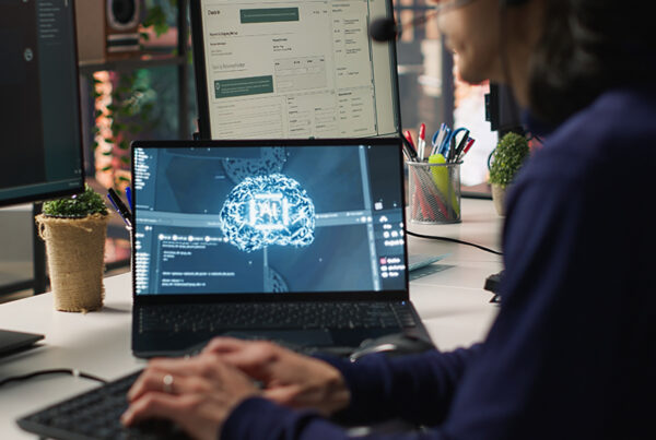 A person working on a laptop displaying an AI brain graphic, with multiple monitors and a modern workspace setup, representing Retrieval-Augmented Generation technology.